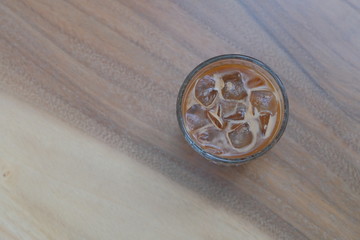 top view of a glass of iced coffee on patterned wooden table. blur background