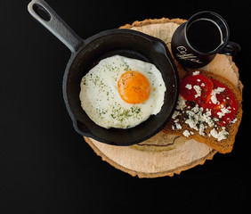 Fried eggs in a cast-iron frying pan, a sandwich with tomato and feta cheese, a coffee mug.