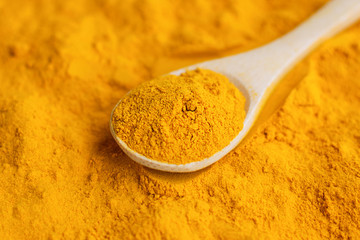 Close-up turmeric powder in wooden spoon at scattered curcuma.