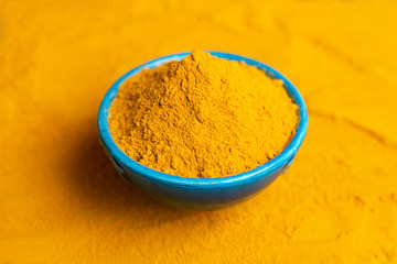 Turmeric powder in blue bowl at orange background.