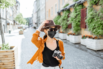 Young female tourist in facial protective mask walking with photo camera on the old city street....