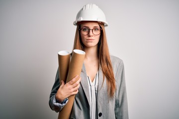 Young beautiful redhead architect woman wearing glasses and safety helmet holding blueprints with a confident expression on smart face thinking serious