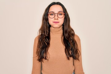 Young beautiful woman wearing casual turtleneck sweater and glasses over white background puffing cheeks with funny face. Mouth inflated with air, crazy expression.