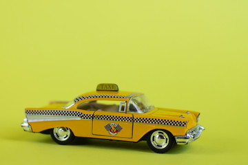 A yellow toy taxi car on a pastel yellow background. Taxi service.