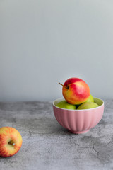 Green and red organic healthy apples in pink bowl on grey board
