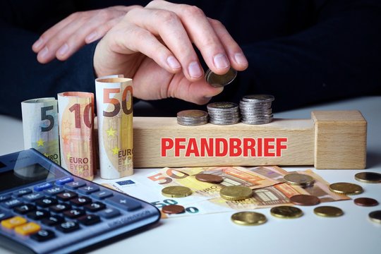 Pfandbrief. M&auml;nnliche Hand stapelt Geld-Turm (Euro). Begriff an Baustein. M&uuml;nzen, Scheine & Taschenrechner. Konzept f&uuml;r Business, Finanzen, Statistik