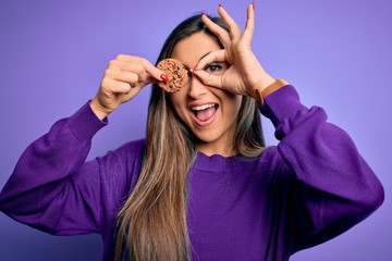 Young beautiful brunette woman holding healthy chocolate cookie over eye with happy face smiling...