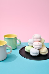 Top view of pastel colored marshmallow on black plate and two empty cups on a blue pink background. Minimalism photo for your design