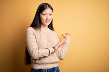 Young beautiful asian woman wearing casual sweater over yellow isolated background Inviting to enter smiling natural with open hand