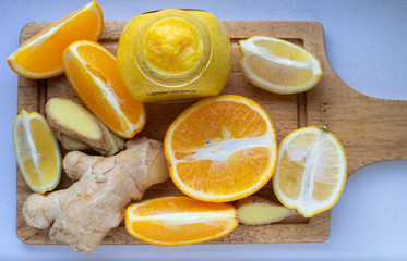 Jar of orange and lemon jam with honey and ginger on a cutting board and slices of lemon and orange