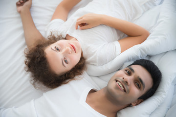 Obraz na płótnie Canvas Handsome young men and beautiful women wearing white T-shirts They are smiling, looking and lying on the bed in the bedroom. The concept of morning sleep for lovers and love
