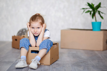 A little blonde girl plays at home in quarantine with cardboard boxes. The child moves to a new apartment, is happy and happy.