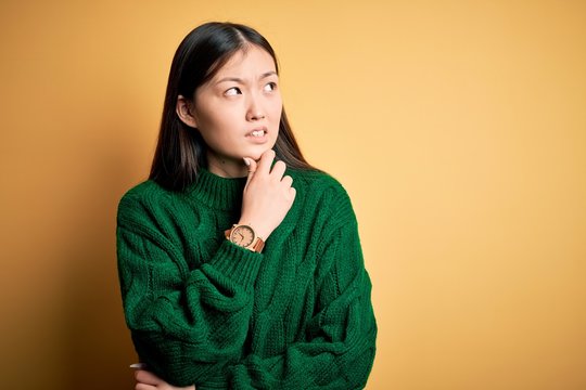 Young beautiful asian woman wearing green winter sweater over yellow isolated background Thinking worried about a question, concerned and nervous with hand on chin