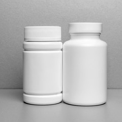 2 white jars for medicines and vitamins and dietary supplements without a name are on a gray shelf. copy space to the left. layout for a pharmacy, a store