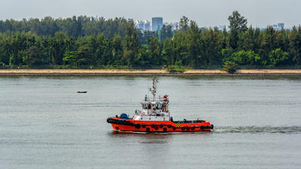 Tugboat underway along the Singapore island shoreline in Johor strait.