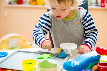 Cute girl playing with many colorful doughs.