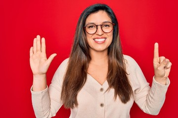 Young hispanic smart woman wearing glasses standing over red isolated background showing and pointing up with fingers number six while smiling confident and happy.