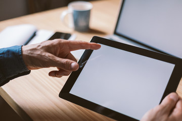Male hand pointing at tablet white screen. Mockup of laptop and tablet screen. Modern organic wooden environment