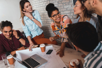 Group of modern business people in casual wear discussing architectural designs while sitting in the creative office.