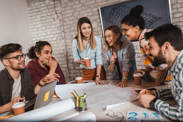Group of modern business people in casual wear discussing architectural designs while sitting in the creative office.