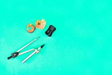 Two pencil shavings ,pencil sharpener and a silver color wood pencil attached to a pencil compass placed on a blue background