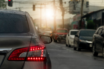 Rear side of car on the road with open brake light and with drop of water on body. and blurred of cars stop beside road in the city.