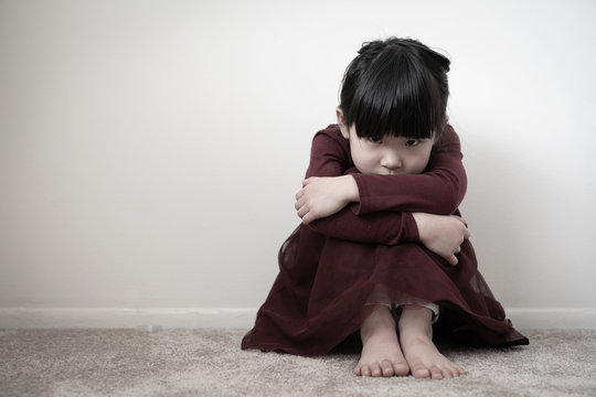 Lonely sad young girl is sitting in the corner wall and holding her knees, concept of domestic violence, abuse and harassment