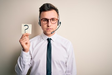 Young call center operator man wearing headset holding paper note with question mark with a...