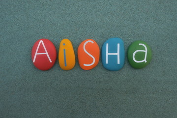 Aisha,  Arabic female given name composed with multi colored stone letters over green sand