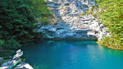Unique Blue Lake in Abkhazia. A small but deep lake of turquoise and aquamarine color is surrounded by sheer white cliffs. On the shore of peacocks with bright plumage. Reflection in water.