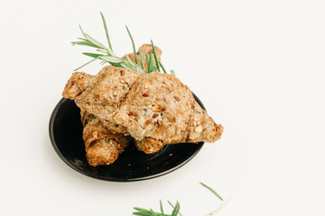 Cozy wheat croissants with sesame seeds in a dark plate isolated on white.