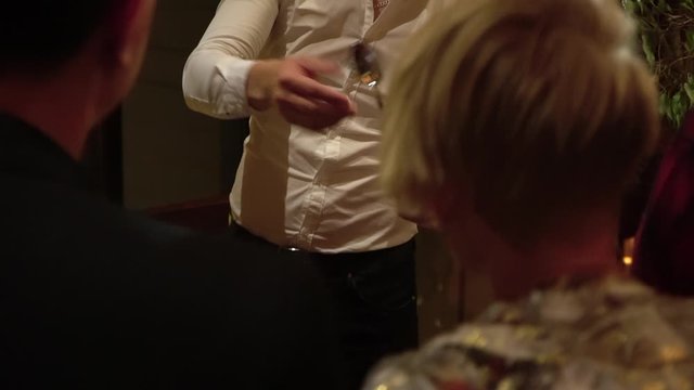 A male magician shows magic with his hands with an object. Bends the spoon. Artist in a white shirt with a gold jelly.