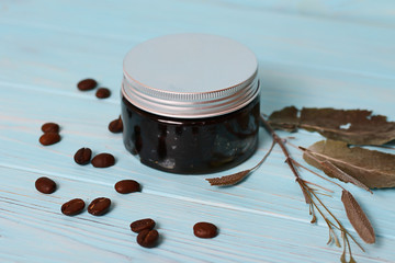 Plastic container with natural cosmetics on a wooden background.Grains of coffee and field herbs on the backdrop.