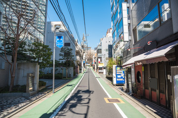 Naklejka premium Narrow street lined with apartment buildings and restaurants in central Tokyo on a clear spring day
