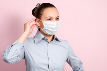 Studio portrait of young woman wearing a face mask, looking at camera, close up, isolated on pink background. Flu epidemic, dust allergy, protection against virus