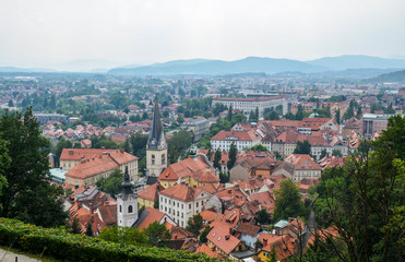 Fototapeta premium Aerial view of the old city Ljubljana, the capital of Slovenia. Buildings with red tile roofs, mountain range in the background, seen from city castle hill