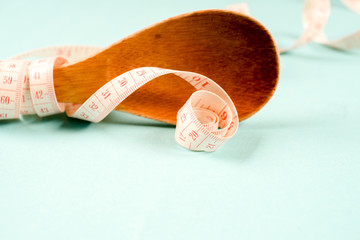 Wooden spoon with a measuring tape on a blue background, diet, healthy lifestyle.