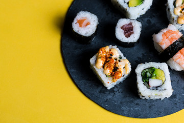 Slate plate with prawn sushi, avocado, raw fish, rice and salmon, on a yellow background
