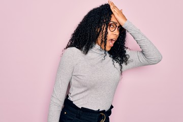 Young african american woman wearing turtleneck sweater and glasses over pink background surprised...