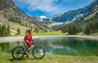 Obraz premium pretty senior woman riding her electric mountain bike at the Seealp lake in the Nebelhorn area above Oberstdorf, Allgau Alps, Bavaria, Germany 