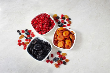 Different dried fruits: prunes, dried apricots and cherries in a bowls on a light background, top view.