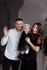 Portrait of beautiful young parents and their cute little daughter hugs, looking at camera and smiling indoors. mother's, father's, baby's day. concept of family. family look
