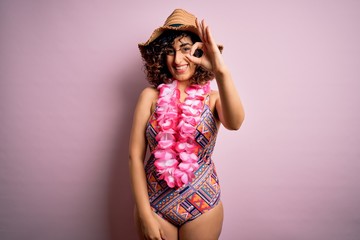 Young beautiful arab woman on vacation wearing swimsuit and hawaiian lei flowers smiling positive doing ok sign with hand and fingers. Successful expression.