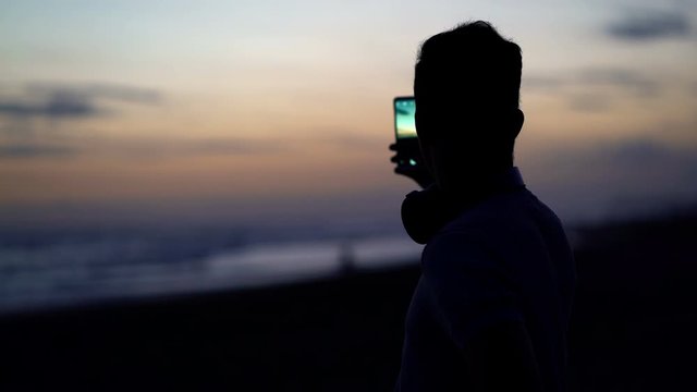Silhouette of man taking photo of sunset on beach