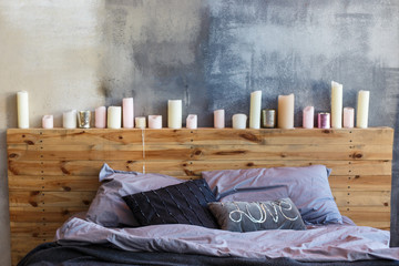 Stylish bedroom in loft style with grey colors and many candles. Bed with dark grey blanket