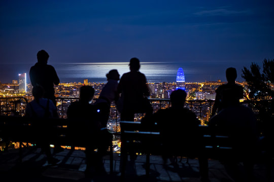 Barcelona saliendo del confinamiento, vista de la ciudad iluminada desde el parque del Guinardo, con varias persona apreciando la ciudad iluminada por la luna llena