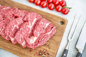 Fresh raw beef steaks with pepper and tomatoes on wooden cutting board. Top view.