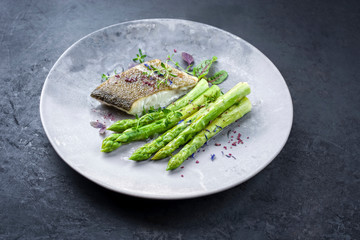 Gebratenes Gourmet Skrei Kabeljau Fisch Filet mit grünem Spargel und Salat angeboten als closeup...