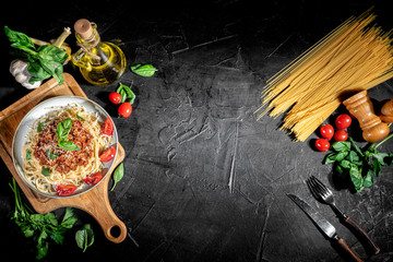 Heaped plate of delicious Italian spaghetti pasta with fresh basil leaves and grated parmesan cheese on dark background