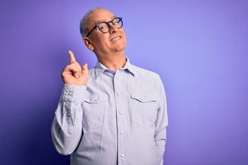 Middle age handsome hoary man wearing striped shirt and glasses over purple background with a big smile on face, pointing with hand and finger to the side looking at the camera.